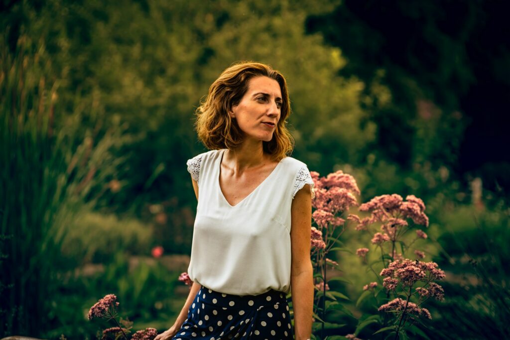 Elle détourne le regard, enveloppée par la verdure et les fleurs sauvages.