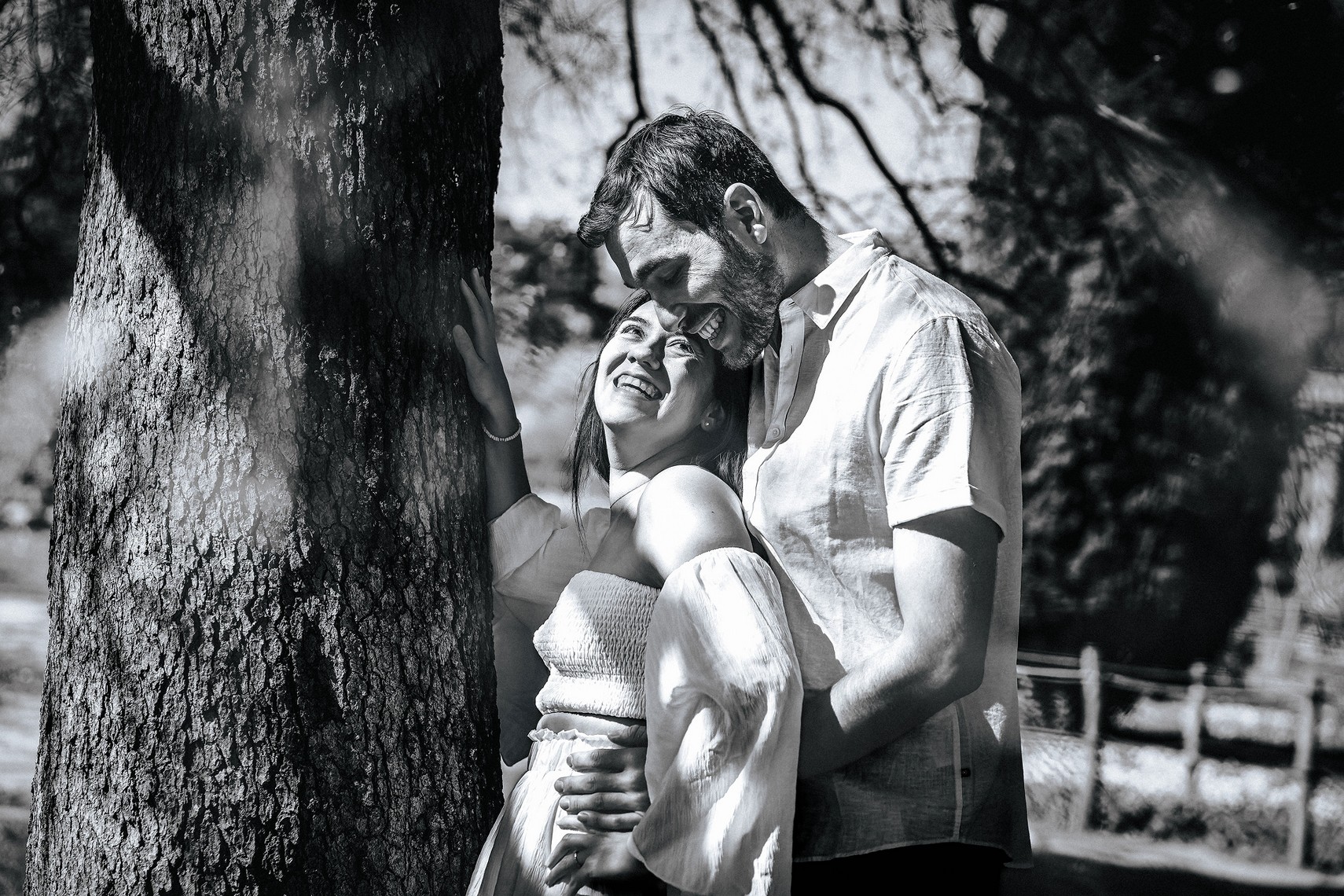 Couple avec un moment complice posant près d'un arbre